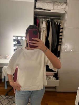 Stickad tröja tshirt  - Säljer en vit topp med ribbade detaljer och vida, halvlånga ärmar. Toppen har en avslappnad passform och är perfekt till jeans eller kjol. Materialet känns mjukt och bekvämt mot huden.