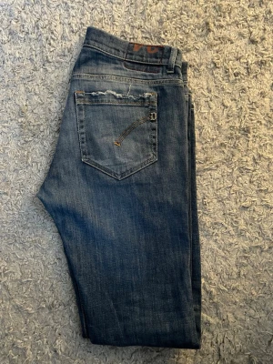 Blå jeansbyxor från Dondup med raka ben - Säljer ett par klassiska blå jeans från Dondup i modellen GEORGE, med raka ben och snygga slitningar på bakfickorna. Priset är inte spikat, Jeansen har fem fickor, mörk tvätt som ger en cool vintagekänsla. Perfekta för dig som gillar en tidlös och avslappnad stil. De är ner suydda till W28-W29 tidigare varit w33 tror jag!