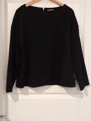 Svart långärmad topp från H&M - En enkel och stilren svart långärmad topp från H&M. Toppen har en rak passform och rund halsringning, vilket gör den lätt att matcha med olika outfits. Dragkedja på ryggen.