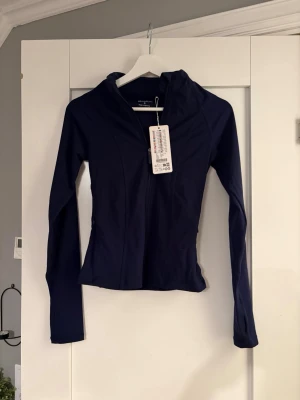 Mörkblå träningsjacka - Snygg mörkblå träningsjacka från New Yorker med åtsittande passform, långa ärmar och dragkedja framtill. Jackan har huva och är tillverkad i ett stretchigt funktionsmaterial som passar perfekt till träning och sportaktiviteter.