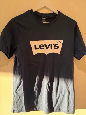 Svart Levi's t-shirt med logga - Snygg svart t-shirt från Levi's med den klassiska vita loggan tryckt på bröstet. T-shirten har rund halsringning och korta ärmar. Tillverkad i mjuk bomull som känns skön mot huden. Perfekt för en avslappnad och stilren look.