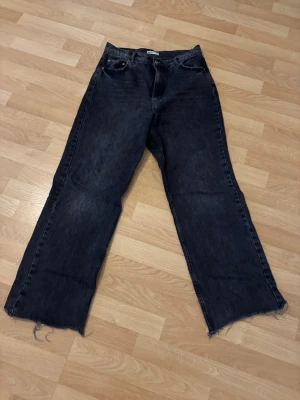 Svarta raka Jeans - Säljer ett par svart/gråa jeans med rak passform, fransig kant nedtill. Jeansen har klassisk femficksdesign och hög midja. Perfekta för en avslappnad och trendig look. Materialet är kraftig denim i bomull.