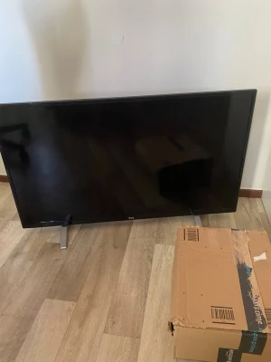 TCL platt-TV svart med metallben - Säljer en svart platt-TV från TCL med stilrena metallben. TV:n har HDMI-ingång och en modern, tunn design som passar perfekt i vardagsrummet eller sovrummet. Baksidan har tydliga anslutningar och etiketter. Perfekt för streaming och gaming.
