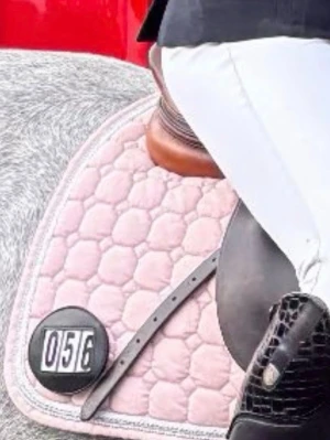 Ljusrosa equiline schabrak med vit och glitter kant - Säljer ett ljusrosa schabrak med vit kant och quiltat mönster, perfekt för tävling eller träning. Lite missfärgad vid sadelgjorden men absolut inget som syns, som man ser på bilden. 