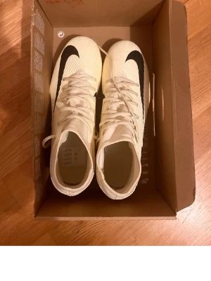Nike Superfly 8 Club fotbollsskor - Säljer ett par Nike Superfly 8 Club fotbollsskor i stilren vit färg med svart swoosh. Skorna har högt skaft och snörning för bra passform. Tillverkade i syntetmaterial som ger bra bollkontroll och grepp på planen. Perfekta för dig som vill sticka ut på matchen. Helt nya använts en gång. Priset går att diskuteras!!
