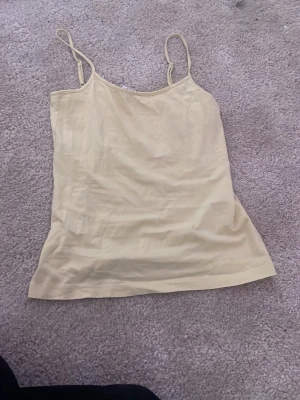 Beige linnetopp med smala axelband - Enkel och stilren ljus gul linnetopp med smala axelband. Perfekt för varma dagar eller som lager under andra plagg. Tunn och mjuk känsla, lätt att matcha med olika outfits.