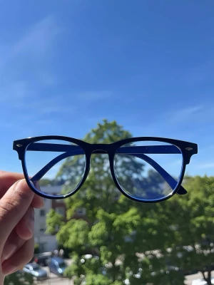 Svarta glasögon  - Snygga solglasögon med svart båge och blåtonade glas. Klassisk rundad form som ger en cool vibe. Perfekta för soliga dagar och passar till de flesta outfits. Bågarna är i plast och har en stilren look.