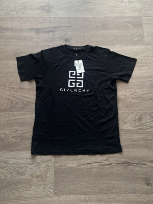 Svart Givenchy t-shirt med logga - Snygg svart t-shirt från Givenchy med stor vit logga och grafiskt tryck på bröstet. Klassisk passform med korta ärmar och rund halsringning. Tillverkad i mjuk bomull som känns skön mot huden. Perfekt för dig som gillar stilrena designer.
