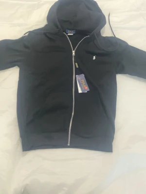 Polo Ralph Lauren Zip Hoodie – Svart - 🖤 Polo Ralph Lauren Zip Hoodie – Svart 🖤  Stilren och bekväm hoodie från Polo Ralph Lauren ✨ Den svarta designen tillsammans med den klassiska loggan ger en clean och exklusiv look.  ✔️ Dragkedja framtill ✔️ Mjuk och skön passform ✔️ Praktiska fickor ✔️ Perfekt för vardag och streetwear 😎  📏 Storlek: S 🎨 Färg: Svart 🔥 En tidlös hoodie som passar till allt!