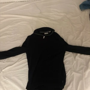 Svart tröja med halv dragkedja - Svart långärmad tröja från Jack&Jones med halv dragkedja vid halsen och hög krage. Enkel och stilren design, perfekt för lager-på-lager. Passar dig som gillar sportig och clean stil.