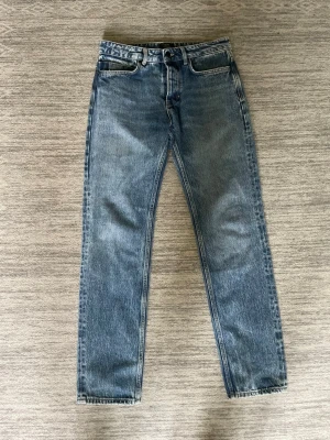 Blå NEUW jeans - Ett par blå jeans med rak passform och hög midja. Jeansen har fem fickor, bälteshällor och stängs med knapp och dragkedja. Tillverkade i slitstark denim med en snygg tvättad look. Perfekta till en avslappnad stil.