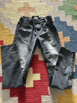 Grå jeans av RYVLS - Säljer ett par grå jeans från RYVLS ben och klassisk femficksdesign. Jeansen har en snygg tvätt med ljusare partier och är tillverkade i ett mjukt denim-material. Perfekta för dig som gillar en enkel och stilren look.