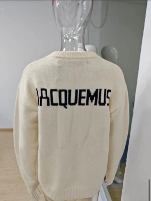 Vit stickad tröja från Jacquemus - Säljer en stilren vit stickad tröja från Jacquemus med svart logotyp på ryggen. Tröjan har rund halsringning och ribbade muddar vid ärmslut och nederkant. Perfekt för dig som gillar minimalistisk design och vill ha något trendigt i garderoben. Passar både large och medium. Aldrig använt 