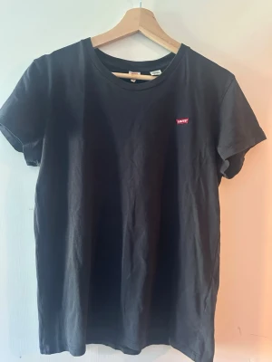 Svart/mörkblå t-shirt från Levi's - Klassisk svart t-shirt från Levi's med liten röd logotyp på bröstet. T-shirten har rund halsringning och korta ärmar. Perfekt basplagg i mjuk bomull som passar till allt. Står M men passar S