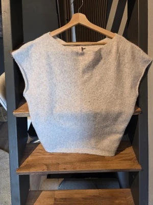 Ljusbeige ärmlös top - En beige stickad tröja med båt halsringning och ärmlös design. Tröjan har ribbad nederkant och är gjord i ett mjukt material som passar perfekt för lager-på-lager. Enkel och stilren look. Storlek M