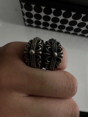 Chrome hearts ringar - Säljer stainless steel metal ringar med ett detaljerat korsliknande mönster och rundad mitt. Ringarna har en robust och unik design som sticker ut och passar perfekt för dig som gillar statement-smycken.