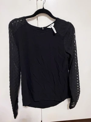Svart långärmad topp med spetsärmar - Snygg svart blus från zalando med långärmade spetsärmar som ger en elegant touch. Toppen har rund halsringning och är i ett mjukt material som känns skönt mot huden. Perfekt att styla med både jeans och kjol.