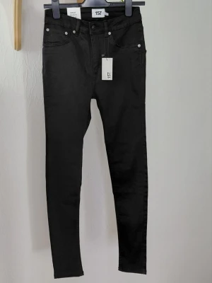 Svarta skinny jeans  157. M - Snygga svarta skinny jeans från 157 med klassisk femficksdesign och hög midja. Jeansen har smal passform och är tillverkade i stretchigt material för extra komfort. Perfekta att matcha med en hoodie eller crop top. Storlek M. Oanvända. 