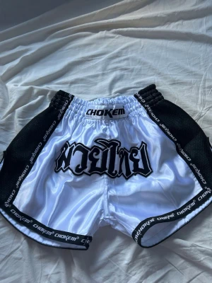 Muay Thai shorts  - Snygga Muay Thai shorts i storlek S från Chokem i blankt vitt material med svarta detaljer. Svart text på framsidan och logotyp längs kanterna. Aldrig använda. 350kr original pris