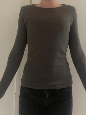 Mörkgrå långärmad topp H&M - En enkel och stilren mörkgrå långärmad topp från H&M Basic i ekologisk bomull. Modellen är figurnära med rund halsringning och passar perfekt till alla typer av outfits. Supermjuk och skön mot huden.