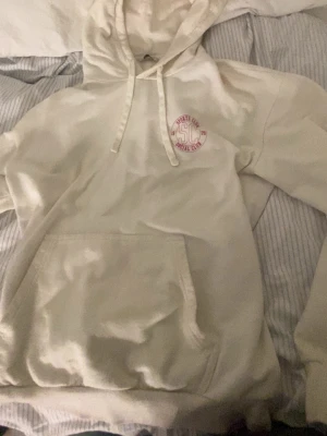 Vit hoodie med rosa tryck på bröstet - Säljer en vit hoodie med huva och dragsnören. På bröstet finns ett litet tryck i rosa med texten 'SC Social Club'. Hoodien har en stor magficka och är gjord i mjukt material, Köpt själv på en secondhand och använt max 2-3 gånger. Själv vet jag inte hur mycket personen jag köpt av använt tröjan🤍