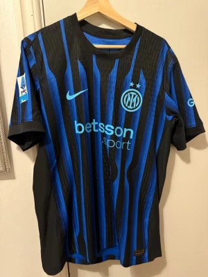 Inter Milan matchtröja Nike blå/svart - Snygg Inter Milan matchtröja från Nike i blått och svart med vertikala ränder. Tröjan har klubbmärke, Nike-logga och sponsortryck framtill samt Serie A-märke på ärmen. Perfekt för fotbollsfans som vill visa sitt stöd på läktaren eller planen.
