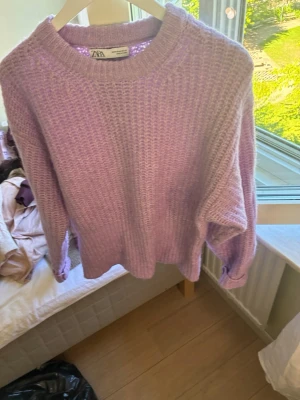Ljuslila stickad tröja från Zara - Mysig stickad tröja från Zara i en trendig ljuslila färg. Tröjan har rund halsringning, ribbade muddar och en avslappnad passform. Perfekt för lager på lager och ger en soft vibe till din outfit.