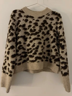 Beige leopardmönstrad stickad tröja H&M - Stickad tröja från H&M i beige med leopardmönster i mörkbrunt och svart. Tröjan har rund halsringning, ribbade muddar och en avslappnad passform. Perfekt för dig som vill ha en trendig och mysig look.