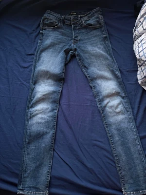 Jack and Jones jeans  - Snygga blå slim fit jeans med lätt slitna detaljer på låren och knäna. Klassisk femficksmodell med normal midja och smala ben. Perfekta för en avslappnad och trendig look.