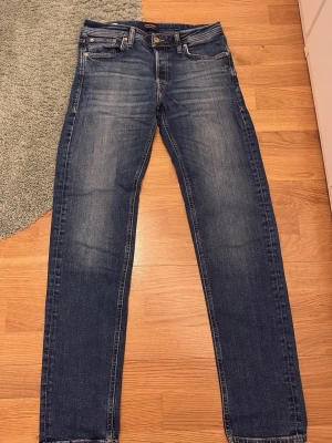 Blå raka jeans från Jack and Jones - Klassiska blå jeans från Jack and Jones med raka ben och fem fickor. Jeansen har en snygg tvätt med lätt slitning på låren och bakficka. Tillverkade i slitstark denim med knappgylf och läderpatch bak i midjan. Hör av er vid frågor!👍