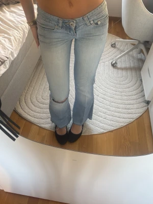 Ljusblå bootcut jeans med slitning - Säljer ett par ljusblå bootcut jeans med låg midja och slitning vid knät. Jeansen har klassisk femficksdesign och är tillverkade i denim med lätt tvättad look. Perfekta för en avslappnad och trendig stil. Super snygga men för korta för mig är 169,5💕