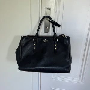 Kate spade väska  - Jättefin handväska från Kate spade. Den är stor och rymlig med flera fack inuti. Den är lite sliten i hörnen och kan finnas nån liten fläck på insidan men annars fint skick! Finns ett långt band så går att ha crossbody om man vill.  Höjd: 25cm Längd: 35cm