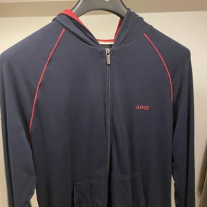 BOSS tröja - En snygg tunnare tröja med dragkedja. Passar bra i storlek. Väldigt snyggt med rött i luvan. Kan sälja billigare om man de är snabb affär. Tvättad och valpaketets innan postad