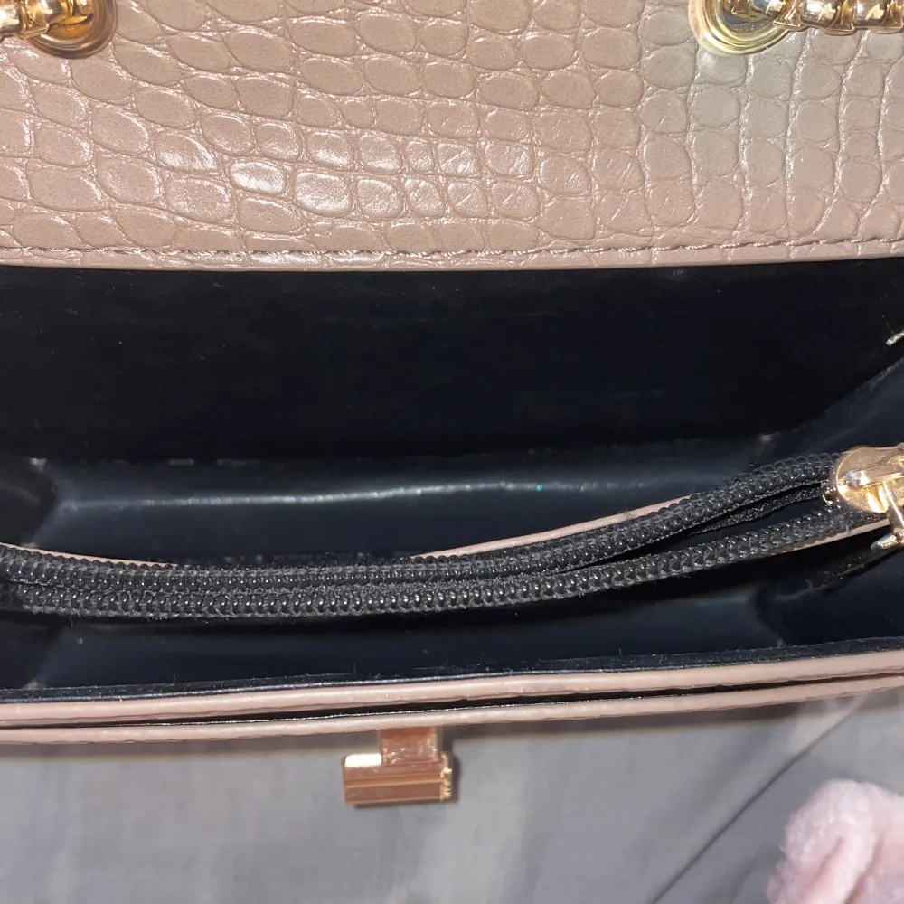 En beige/brun handväska med guld detaljer inte till användning, super fin att ha till klänning . Väskor.