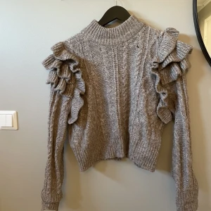 Stickad tröja Gina - Brun stickad tröja med volanger från Gina. Finns ett litet hål, annars i bra skick