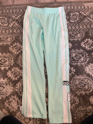 Turkosa adidas byxor - Ett par skitsnygga turkosa adidas buxor som är äkta och sitter midrised. Knappar som man kan knäppa upp vid benen. Säljer för att jag redan har ett exakt likadana💞