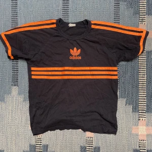 Adidas babytee - Ascool babytee från adidas med bron oranga ränder. Är till för barn så den sitter tight i kragen och ärmarna. Skriv om ni vill ha bild på!