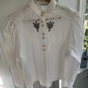 En vit lyxig skjorta med guld knappar och spets. Skjortan är från Grätz i stl 38 och har puff armar 