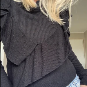 Stickad tröja med volang  - Stickad tröja i svart med volanger. Använd få gånger och inga tecken på användning. Köpare står för frakt.