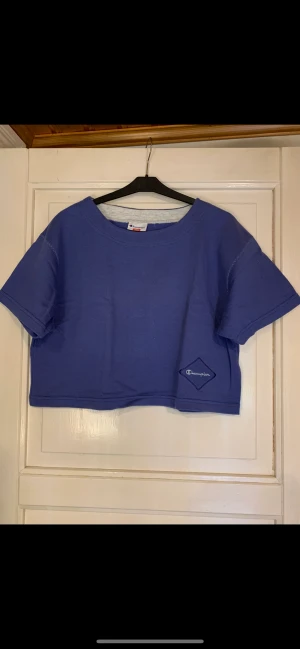 Champion Cropped tröja. St: S, M, L.  - Duvblå tröja / träningströja från Champion. Storlek L men tilläggas hur man vill att den skall sitta. Mått: från ärmhåla till ärmhåla: 2 x 54 cm. Från ärmhåla till nederkant: 20 cm. Hel längd bakstycke: 44 cm. Sänds m Post Nord Spårbart: 60 kr. Skick:Fint