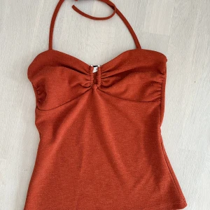 Halterneck topp - BUDGIVNING FRAM TILL LÖRDAG!  Halterneck topp från Gestuz i en orange-röd färg. Samma modell som sista bilden men annan färg (original pris 699kr). Använd endast två gånger, bra skick. Knyts runt nacken + silikonband vilket gör att toppen inte glider ner.