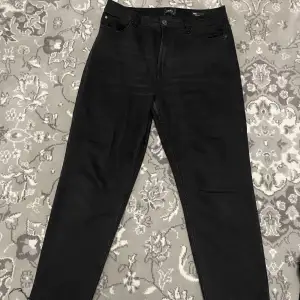 Ett par svarta raka jeans med detaljer i slutet på byxbenen. 