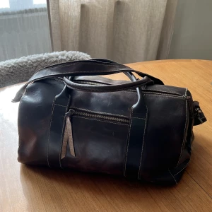 Canvas duffle bag  - Väskan är i fin brun färg och har flertalet förvaringsutrymmen både på ut- och insidan. Den har används vilket är synligt, inget man stör sig på. Nypris ca 1700:-. Vågar ej svara på vad för material men gissningsvis läder. L: 40cm B: 20cm H: 22cm