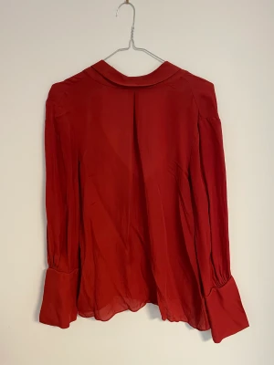 Röd blus  - Röd blus från Massimo Dutti. Tunnt tyg som faller sjukt snyggt. Välanvänd men mycket kvar att ge. Polokrage med knyt baktill. Har även använt den bak och fram för annan design. Mörkt röd blus som gett mycket komplimanger! Jag är st 36-38 och 162 lång. 