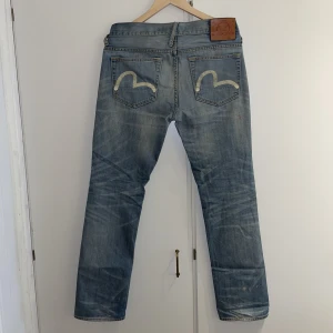 Evisu-jeans - Evisu-jeans från Genes-kollektionen i stl 31R. Givetvis äkta.  Något slitna ”i kanterna” men tyget håller hög kvalitet och det finns ännu mycket liv kvar i dem. Några mindre fläckar från sprayfärg/cement finns.   Nypris över 2500kr. Öppen för bud.