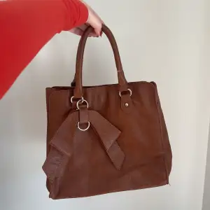 En brun superfin väska med rosett - Går att sätta dit en längre kedja/band om man vill - Köparen står för frakten - Inga returer - Betalning via köp direkt 