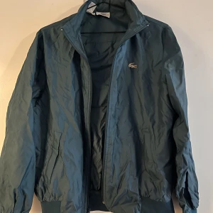 Lacoste winbreaker  - Lacoste windbreaker med inrullad huva. Står storlek L men är mer en Xs/S beroende på hur man vill ha den. 