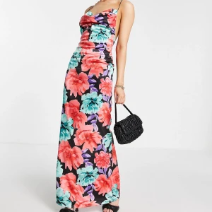 Blommig långklänning med smala axelband - helt ny! - Fantastiskt vacker maxuklänning i färgstarkt blommigt mönster. Drapering över bysten. Lågt skuren i rygg med korsade axelband. Mjuk satin.   Strl 32, men toppen även på 34.  Oanvänd med lappar kvar då den tyvärr inte satt så bra på mig (+ full garderob..)