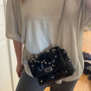 Svart väska med nitar - En svart medelstor väska som man får plats med typ allt i, man kan både ha den på axeln och hängandes. Använd ungefär 3 gånger. Köpt för 250kr.    Kunden står för frakt: 39kr