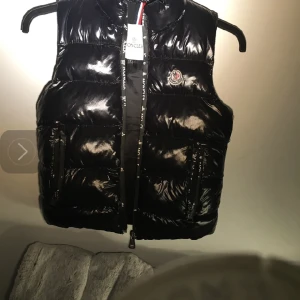 Moncler jackväst barn - Marinblå väst, storlek 32, fodrad ärmlös design, logotypmärke framtill, foder av dunfjädrar, trattformad krage.  